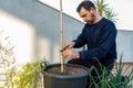 Attractive bearded man in dark clothing transplanting a tomato plant sprout into a larger pot in his urban garden set up on the Royalty Free Stock Photo