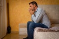 Attractive bearded man depressed and upset in the bedroom. Dramatic 30-40 year old lifestyle portrait, handsome man sitting on bed