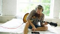 Attractive bearded man sitting on bed learning to play guitar using tablet computer in modern bedroom at home Royalty Free Stock Photo