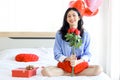 Attractive and beautiful Asian woman holding red rose bouquet while sitting on white bed in bedroom, happy smiling girl holding Royalty Free Stock Photo