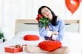 Attractive and beautiful Asian woman holding red rose bouquet while sitting on white bed in bedroom, happy smiling girl holding Royalty Free Stock Photo