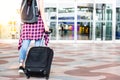 Attractive beautiful traveler woman is waking to airport and dragging suitcases, carrying backpack in front of gateway. Charming