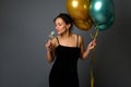 Attractive sexy woman in evening dress holds festive shiny air balloons and drinks sparkling wine from glass isolated over gray Royalty Free Stock Photo