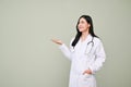 Attractive Asian female doctor standing over isolated grey background, open palm