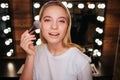 Attractive beautiful young woman look on camera and pose. She stand in beauty room. Woman put blush on cheeks using Royalty Free Stock Photo