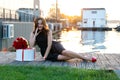 Attractive birthday girl with brown hair in little black dress sitting on the wooden footpath at sunset Royalty Free Stock Photo