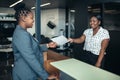 Attractive black receptionist handing over paperwork to businesswoman