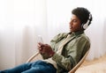 Attractive black teen in headset choosing music playlist on cellphone at home Royalty Free Stock Photo