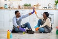 Attractive black woman giving high five to her boyfriend after house cleanup, sitting on kitchen floor, having rest Royalty Free Stock Photo