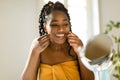 Attractive black woman looking at mirror and using dental floss, cleaning her white teeth, sitting at vanity table Royalty Free Stock Photo