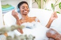 Attractive black woman wearing headphones happy relaxing and dancing in foam bath in bathroom Royalty Free Stock Photo