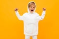 Attractive blond boy in a white hoodie screaming out loud on an orange wall