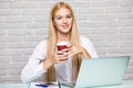 Attractive blond business woman working on her laptop and drinking coffee in her office Royalty Free Stock Photo