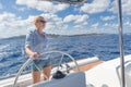 Attractive blond female skipper navigating the fancy catamaran sailboat on sunny summer day on calm blue sea water.