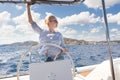 Attractive blond female skipper navigating the fancy catamaran sailboat on sunny summer day on calm blue sea water.