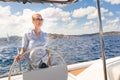 Attractive blond female skipper navigating the fancy catamaran sailboat on sunny summer day on calm blue sea water.