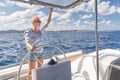 Attractive blond female skipper navigating the fancy catamaran sailboat on sunny summer day on calm blue sea water.