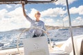 Attractive blond female skipper navigating the fancy catamaran sailboat on sunny summer day on calm blue sea water.