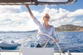 Attractive blond female skipper navigating the fancy catamaran sailboat on sunny summer day on calm blue sea water.