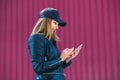 Attractive blond girl in leather black jacket and cap, surfing the Internet on a mobile phone Royalty Free Stock Photo