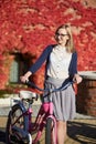 Attractive blond girl at pink lady bicycle on sunny day on wall overgrown with red ivy background. Royalty Free Stock Photo