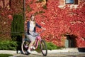 Attractive blond girl at pink lady bicycle on sunny day on wall overgrown with red ivy background. Royalty Free Stock Photo