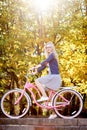 Blond long-haired attractive girl on pink lady bicycle in sunny autumn park on trees background. Royalty Free Stock Photo