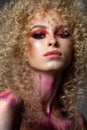 Attractive blond model with a very volume curl hairstyle, colorful red smoky eyes and elements of body art