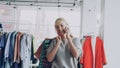 Attractive blond woman is walking between shelves and rails in large store and talking on mobile phone. She is carrying Royalty Free Stock Photo