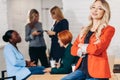 Attractive blonde business woman in red jacket smiling at camera with colleagues working in background Royalty Free Stock Photo