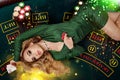 Blonde female in green dress is showing red chips and aces. Lying on playing table with colorful sparkles above her Royalty Free Stock Photo