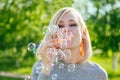 Attractive blonde girl blowing soap bubbles in the park on a background of green grass . bubble and holiday atmosphere Royalty Free Stock Photo