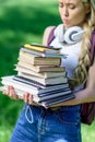 Blonde girl with headphones holding pile of books in park Royalty Free Stock Photo