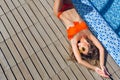 Attractive blonde girl with long hair is lying on flor near pool. She wears orange bikini, sunglasses. She holds hands Royalty Free Stock Photo
