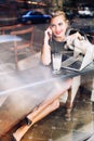 Attractive blonde model through glass window sitting in chair in cafeteria. She speaking on phone, smiling to side.