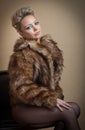 Attractive blonde model with pantyhose, black bra and fur coat posing provocatively on chair. Royalty Free Stock Photo