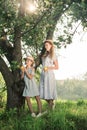 attractive blonde mother and daughter holding appples and posing near tree