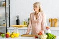Blonde pregnant woman standing near vegetables and fruits in kitchen