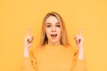 Attractive blonde with a shocking face is isolated on a yellow background, looks at the camera with astonishment and shows fingers Royalty Free Stock Photo