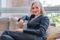 Attractive blonde woman in a business gray suit is sitting on the couch