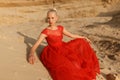 Attractive blonde woman in a red dress lies on the sand, posing in the desert