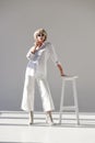 attractive blonde woman in sunglasses and fashionable white outfit leaning on chair Royalty Free Stock Photo