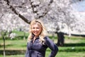 Attractive blonde woman wearing athleisure clothing poses in front of cherry blossom trees