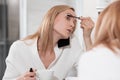 Attractive blonde woman in white bathrobe stands in bathroom by mirror. Applies makeup, speaks on mobile phone and Royalty Free Stock Photo