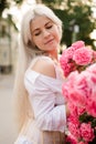 Attractive blonde woman 25 - 29 year old holding pink rose flowers in park outdoors. Healthy natural skin. Spring season. Royalty Free Stock Photo