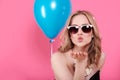 Attractive blonde young woman in elegant party dress and golden jewelry celebrating birthday and blowing a kiss towards camera.