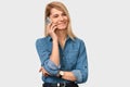 Attractive blonde young woman talking on mobile phone to her friend, looking cheerful and happy, posing on white studio background Royalty Free Stock Photo