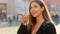 Attractive brazilian girl holding phone speaks with virtual digital voice assistant on smartphone in city street. Happy beautiful Royalty Free Stock Photo