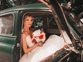 Attractive bride with the bouquet sitting in a vintage car Royalty Free Stock Photo