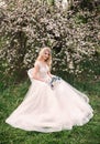 An attractive bride with a bouquet of wild flowers is sitting in a chair in a blooming garden